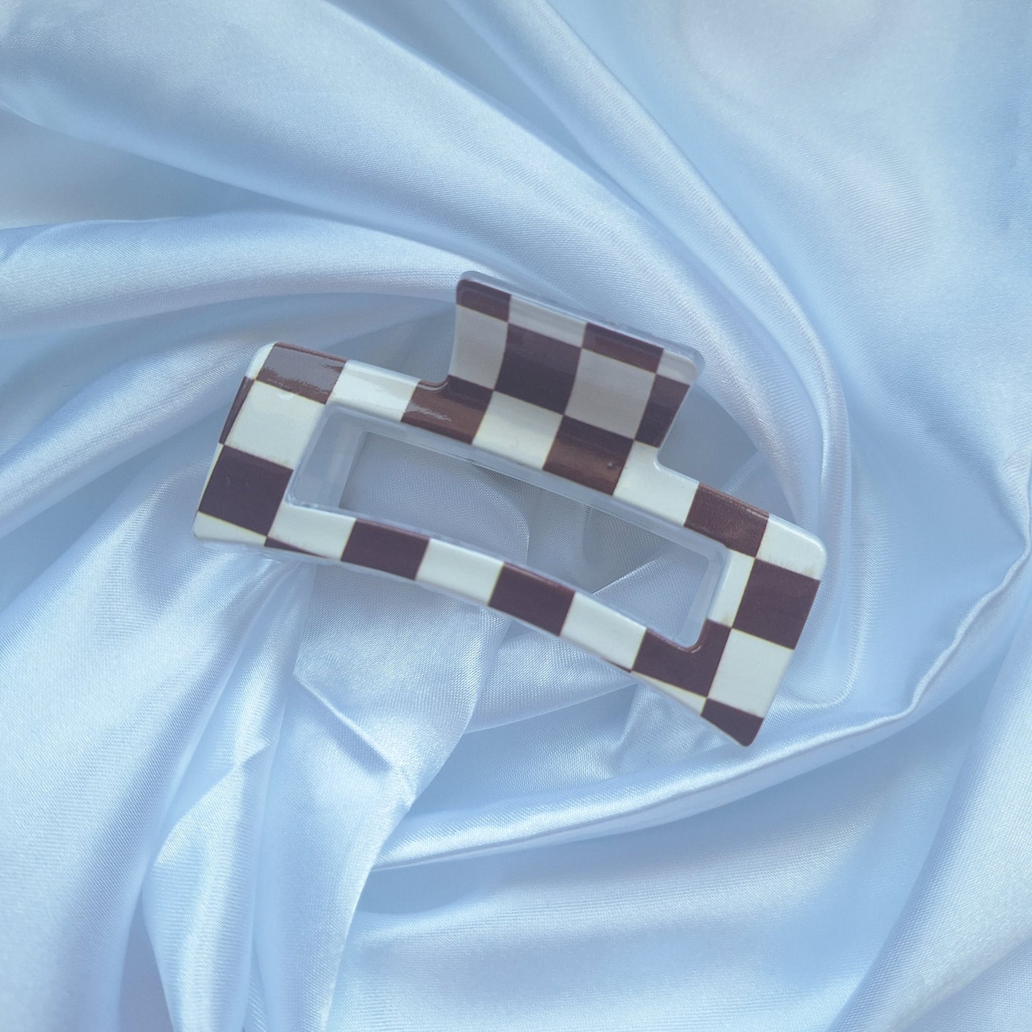 Brown and white checkered acrylic hair claw clip inspired by racing flags displayed on white satin fabric.