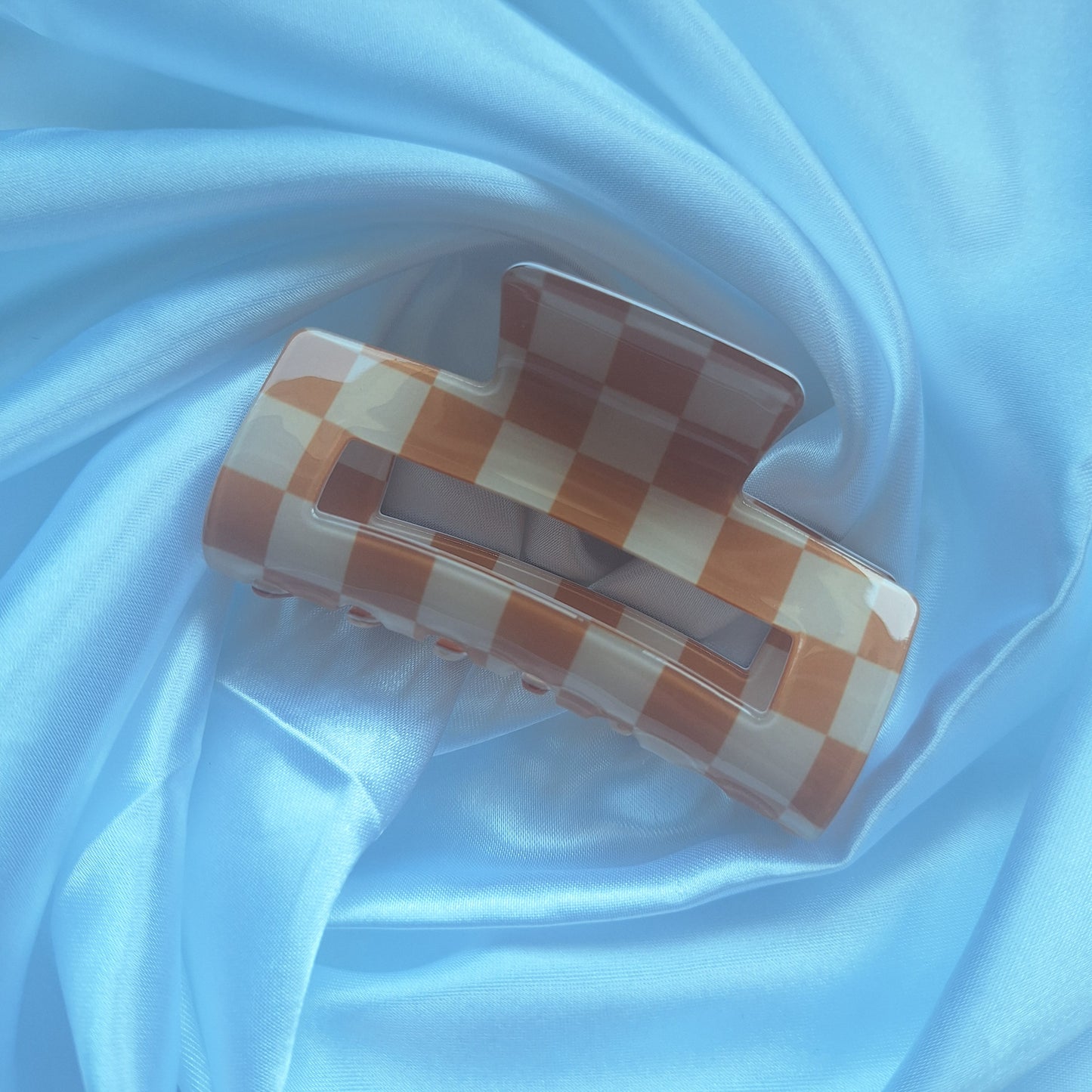 Beige and cream gingham check hair claw clip displayed on a white satin background.