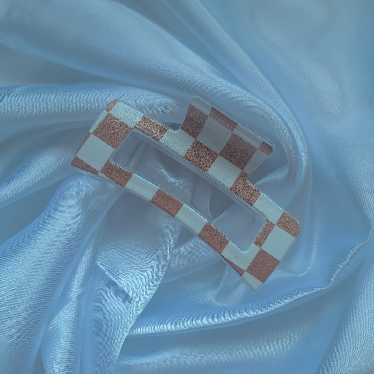 Beige and white checkered acrylic hair claw clip inspired by racing flags displayed on white satin fabric.