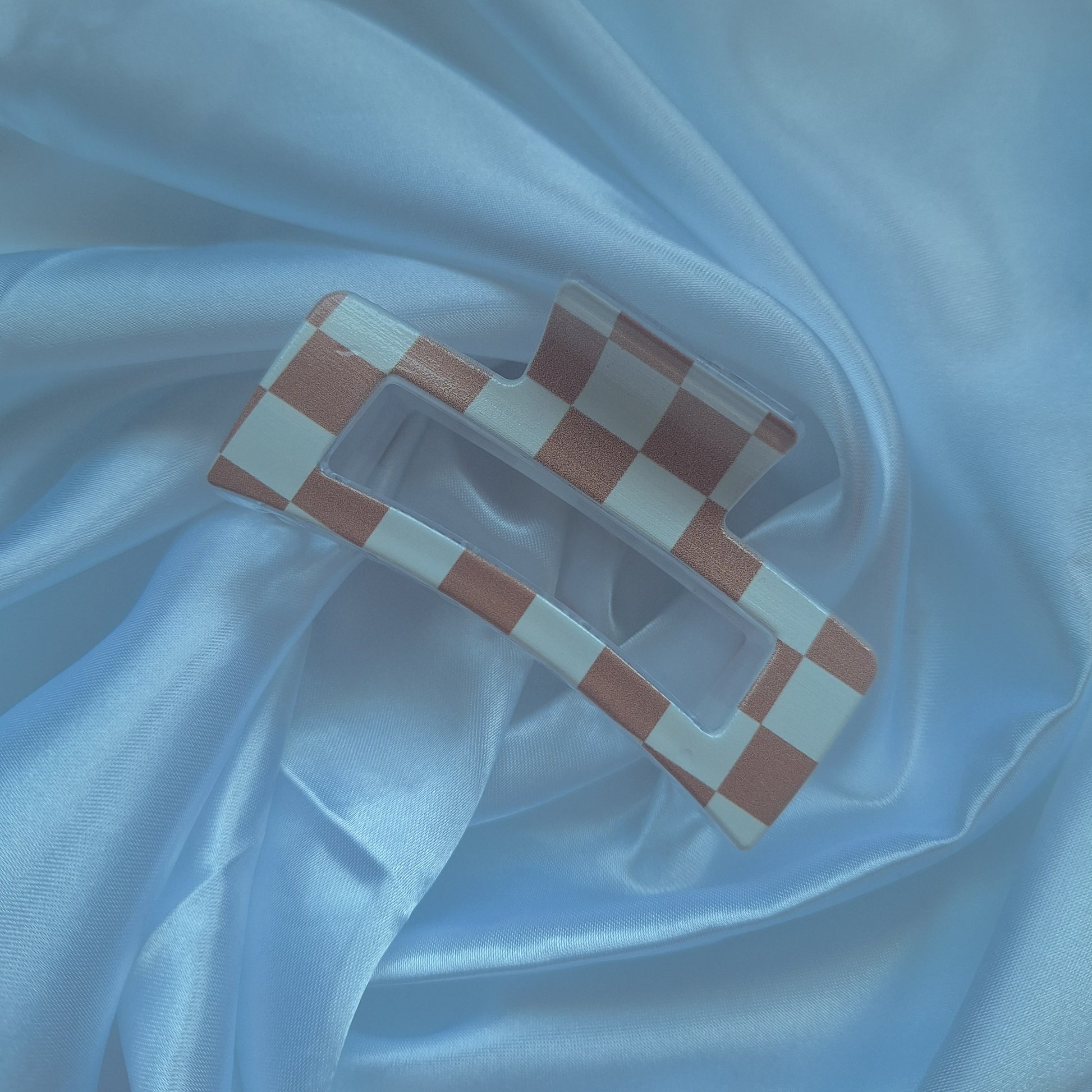 Beige and white checkered acrylic hair claw clip inspired by racing flags displayed on white satin fabric.