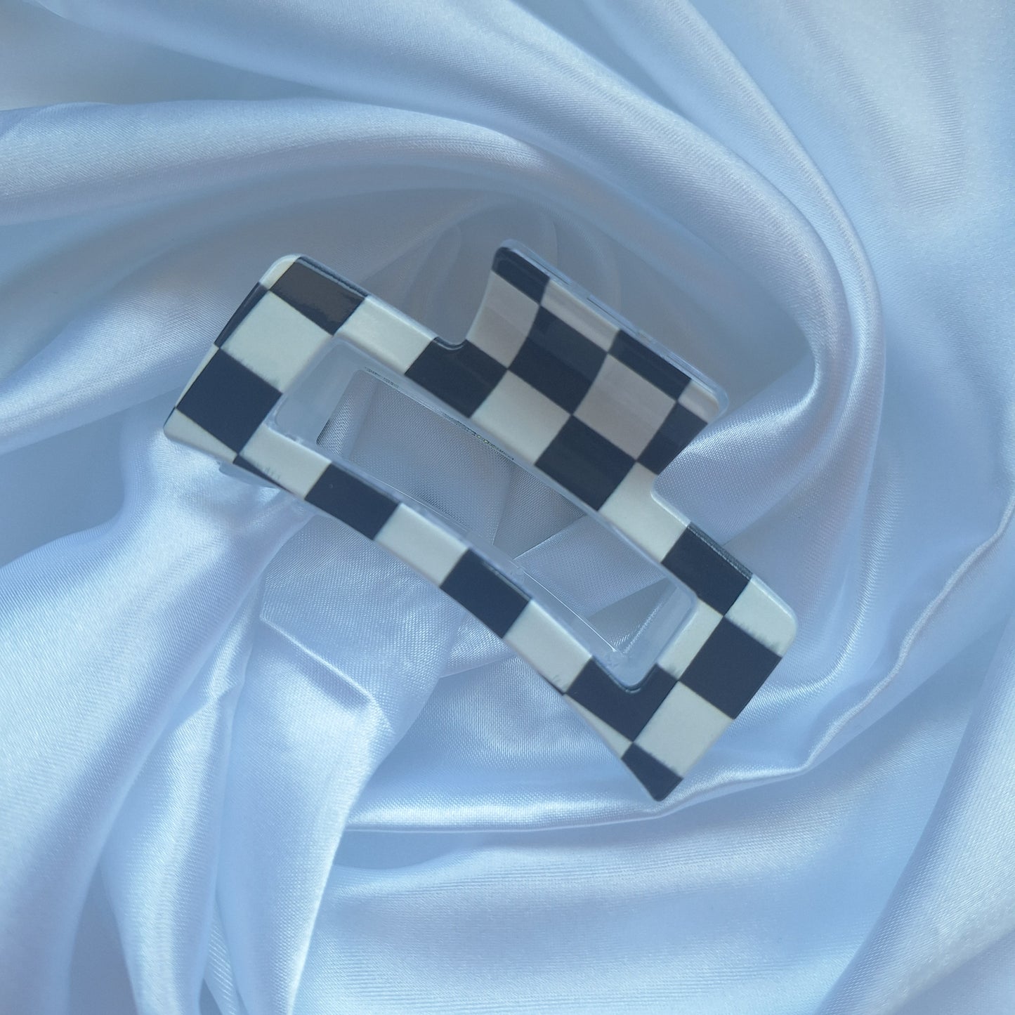 Black and white checkered acrylic hair claw clip inspired by motorsport racing flags displayed on white satin fabric.