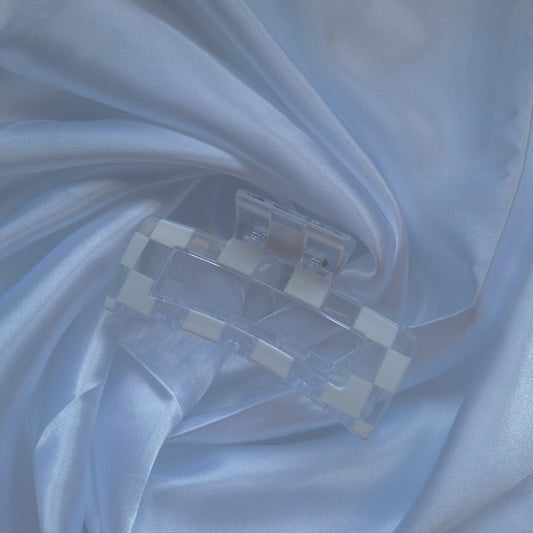 Clear acrylic hair claw clip with white checkered racing flag pattern displayed on white satin fabric.