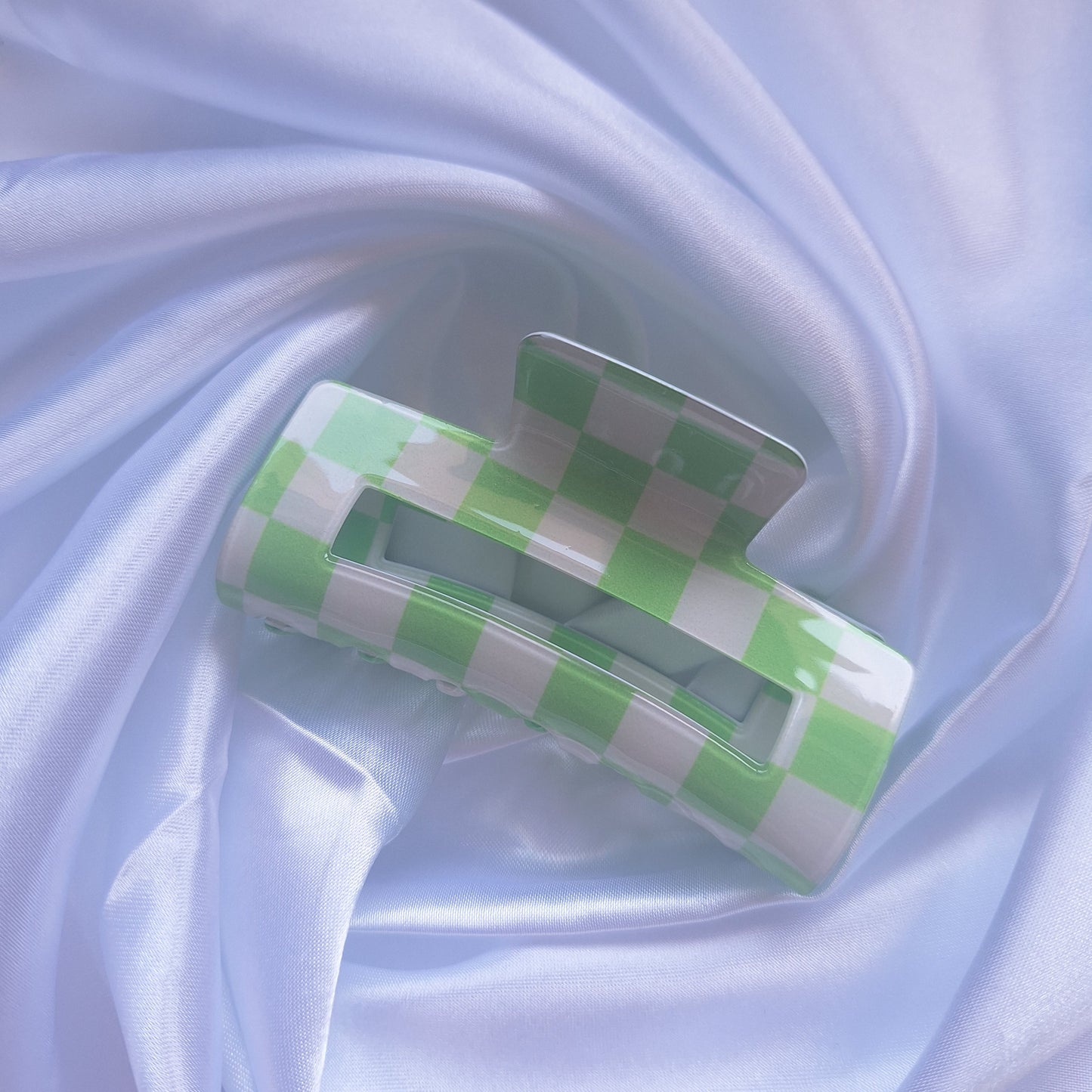Green and white gingham check hair claw clip displayed on a white satin background.