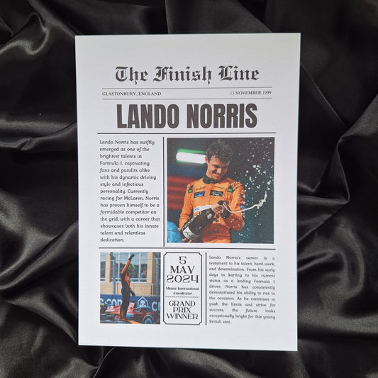 A printed news article featuring Lando Norris, with photographs and text, laid on a black fabric surface.