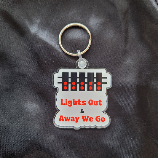 An acrylic keyring with a featuring a white and red design with text 'LIGHTS OUT & AWAY WE GO' on a white background.