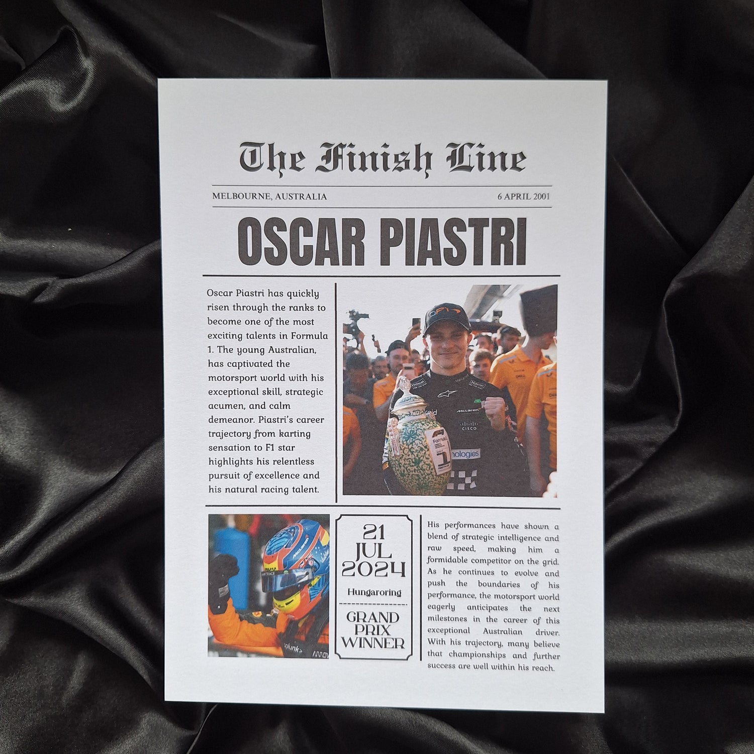 A printed news article print featuring Oscar Piastri, with a black background and text, laid on a black fabric surface.